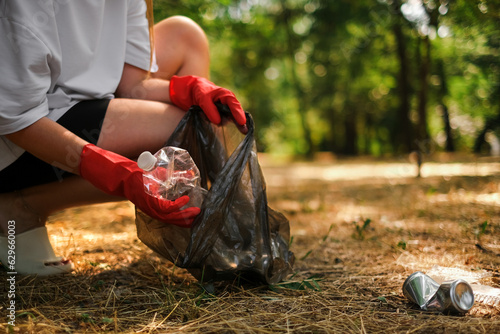 a woman in gloves walks in the park and collects plastic in a trash bag