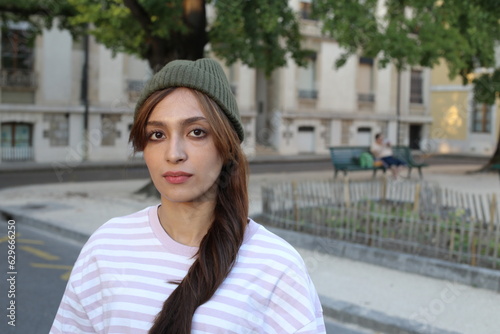 A young fashionable woman in her twenties is wearing a green knitted hat and a pink/white striped shirt 