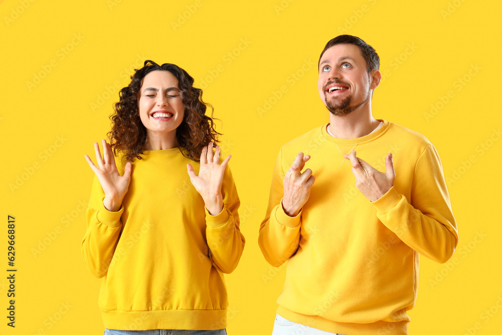 Happy young couple crossing fingers on yellow background Happy young couple crossing fingers on yellow background