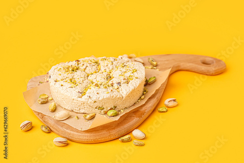 Wooden board of tasty Tahini halva with pistachios on yellow background photo