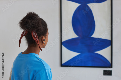 Back view closeup of black teenage girl looking at abstract art in art gallery or museum, copy space