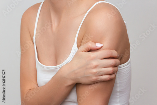a young woman in a white top suffering from shoulder pain, isolated on a light background. A woman's hand holding sore shoulder. Shoulder injury.