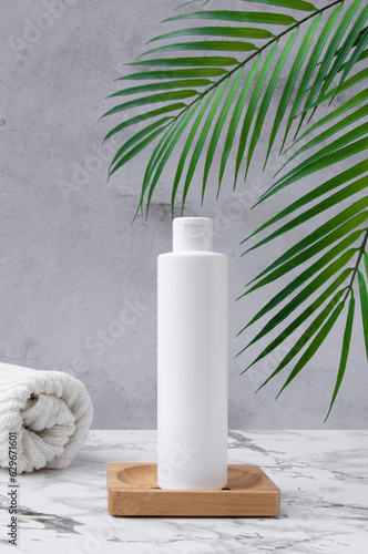 White cosmetic bottle with flip cap with towel and a palm leaves on a wooden table and concrete wall. Sun protection and sunscreen blank product. Beauty skin care product template.