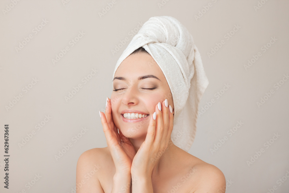 portrait of a young happy beautiful naked woman with closed eyes with a towel on her head smiling and gently touching her face with her hands. Isolated on a beige background portrait of a young happy beautiful naked woman with closed eyes with a towel on her head smiling and gently touching her face with her hands. Isolated on a beige background