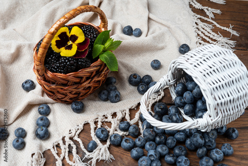 Blackberries and blueberries in small wicker baskets against a white napkin.