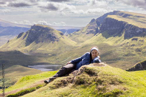 Young woman is lying on the meadow on mountain range Quiraing. It is a geological formation on the Scottish Isle of Skye and a hiker's paradise photo