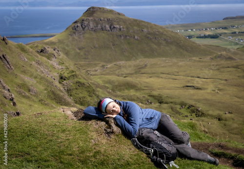 Young woman is lying on the meadow on mountain range Quiraing. It is a geological formation on the Scottish Isle of Skye and a hiker's paradise