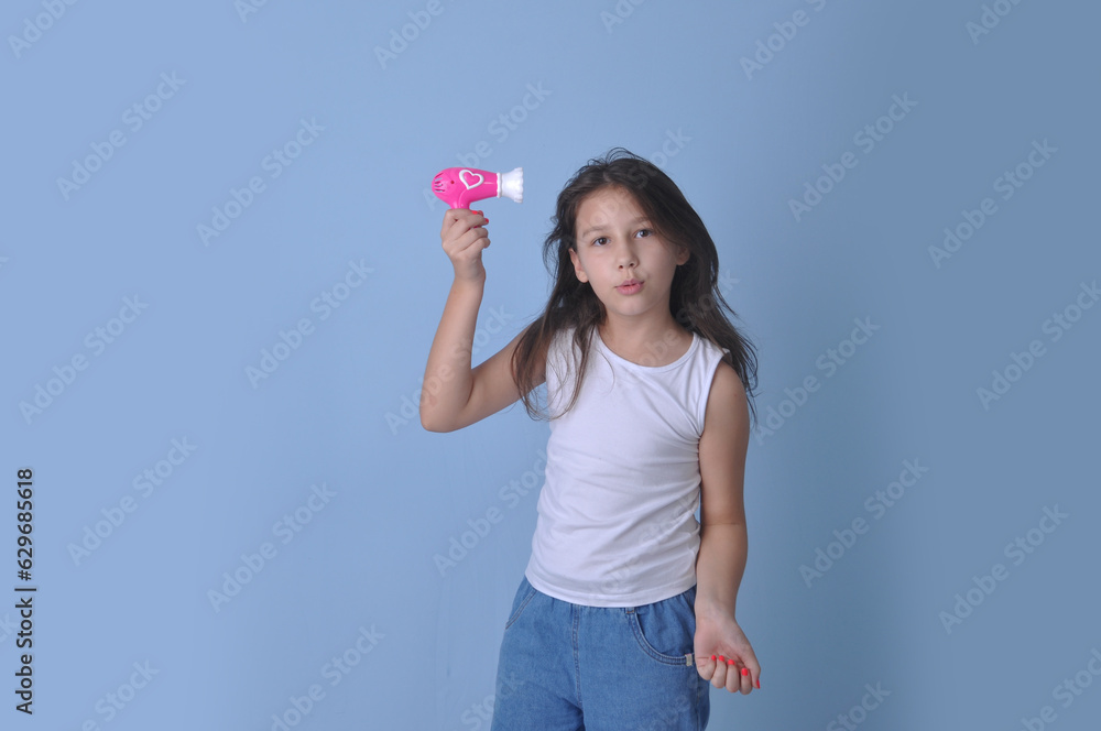 menina pré adolescente segurando secador de cabelo rosa em fundo azul menina pré adolescente segurando secador de cabelo rosa em fundo azul