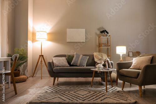 Interior of living room with cozy grey sofa  armchair and glowing lamps