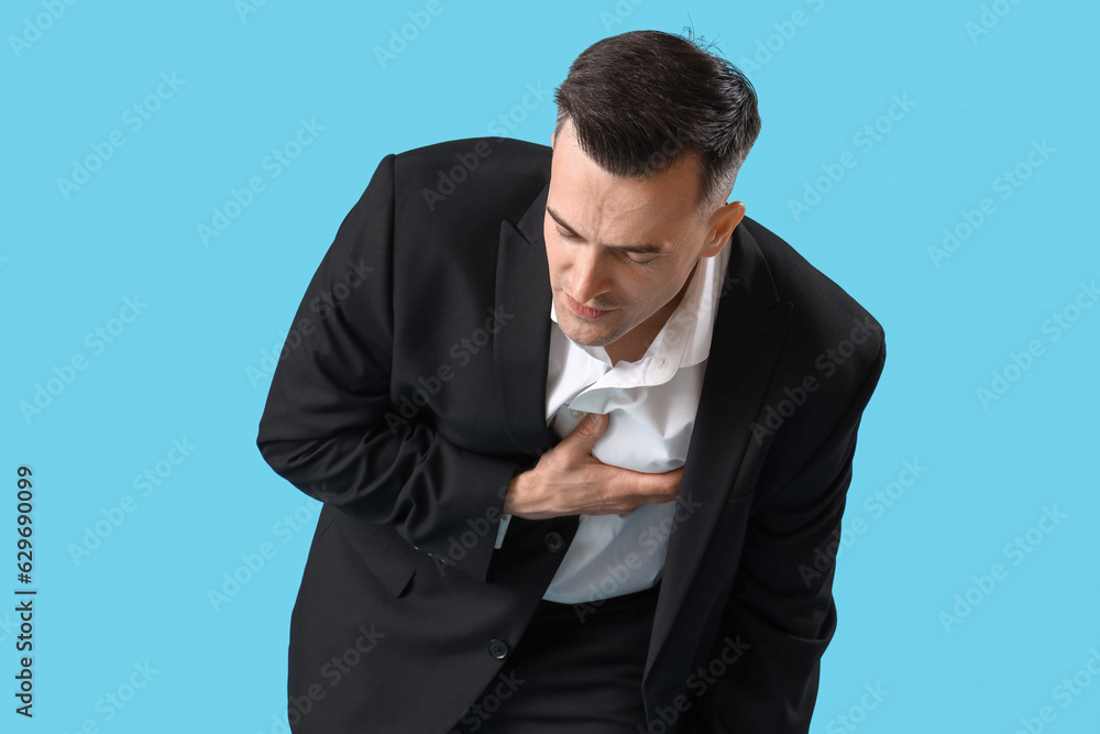 Young businessman having heart attack on blue background