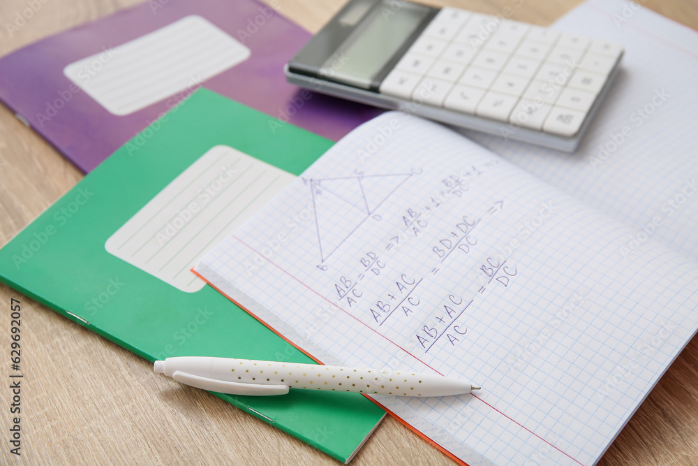 Open copybook with formulas, calculator and pen on wooden table Open copybook with formulas, calculator and pen on wooden table