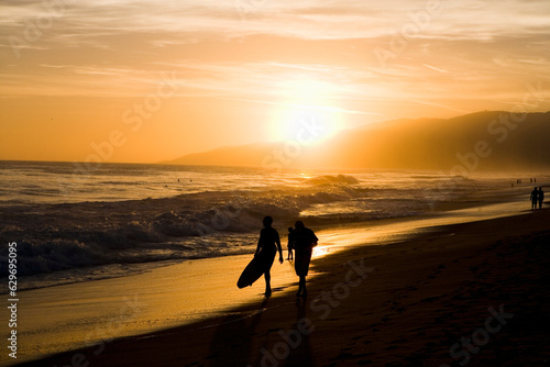 orange sunset on beach with couple walking silhouette