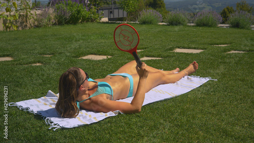 CLOSE UP: Annoying insects attack a young lady who tries to enjoy sunbathing photo