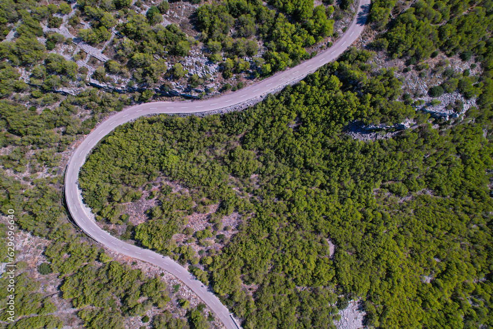 AERIAL TOP DOWN: Curvy asphalt road leading through rugged Adriatic landscape
