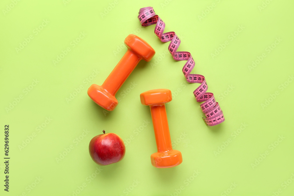 Dumbbells, measuring tape and apple on color background Dumbbells, measuring tape and apple on color background