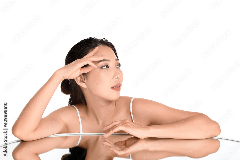 Beautiful young Asian woman with healthy skin and mirror on white background Beautiful young Asian woman with healthy skin and mirror on white background