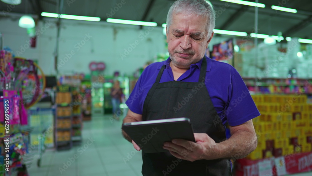 Frustrated Business owner of Supermarket holding tablet inspecting inventory struggling through hard times. Manager of Grocery store feeling stress and anxiety Frustrated Business owner of Supermarket holding tablet inspecting inventory struggling through hard times. Manager of Grocery store feeling stress and anxiety