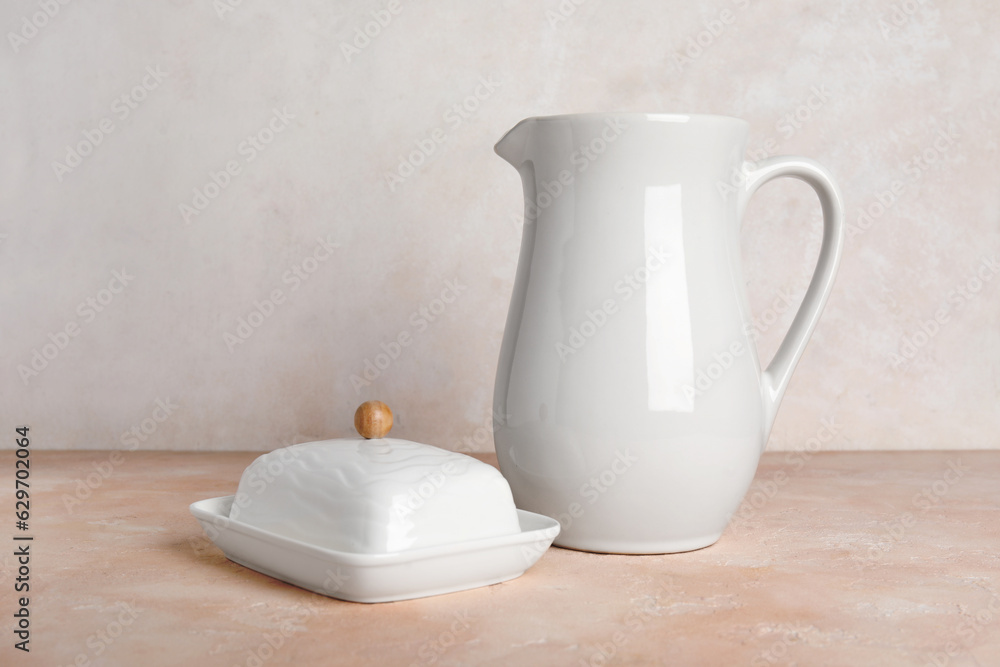 Ceramic butter dish and pitcher on color table against light background Ceramic butter dish and pitcher on color table against light background