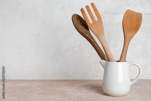 Pitcher with wooden cutlery on light background