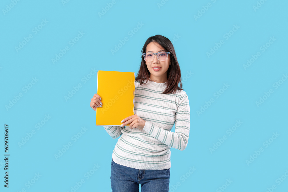 Female Asian teacher with notebook on blue background Female Asian teacher with notebook on blue background