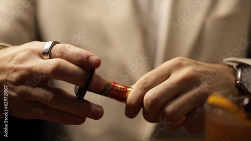 Close-up male hands with a finger are cutting a cigar with a guillotine of scissors on a table
