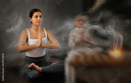 Portrait of sporty smiling young girl sitting in Padmasana yoga position with her arms in namaste during group training in gym