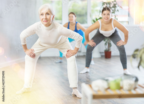 Positive sporty senior woman practicing yoga in group, making stretching asanas for body flexibility