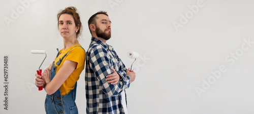 Couple start repair works painting wall together and standing back to back with tools. Happy family make renovation DIY renew home concept. redecorating work in new apartment. banner with copy space