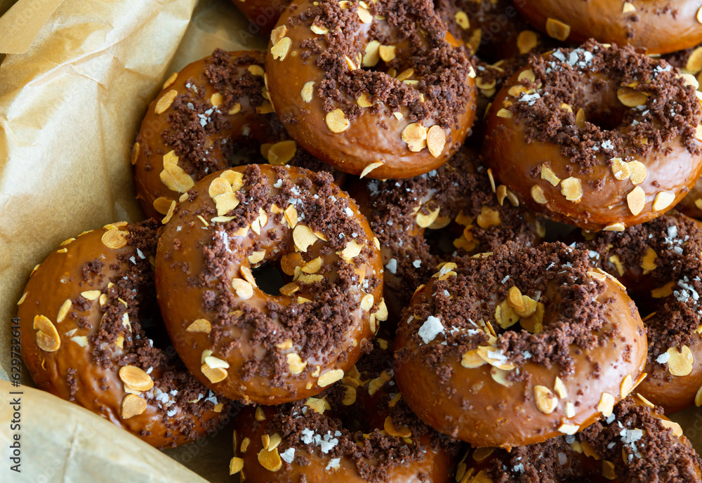 Sweet glazed chocolate donuts decorated with crumbs and almond flakes in box. Fresh pastries showcase