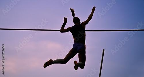 A female pole vaulter (silhouette) jumping with a beautiful sky in the background. Track and field athlete. Young woman pole-vaulting. Pole vault competition photo