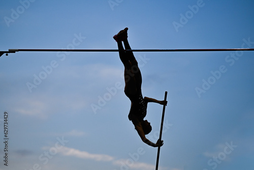 A female pole vaulter (silhouette) jumping with a beautiful blue sky in the background. Track and field athlete. Young woman pole-vaulting. Pole vault competition photo