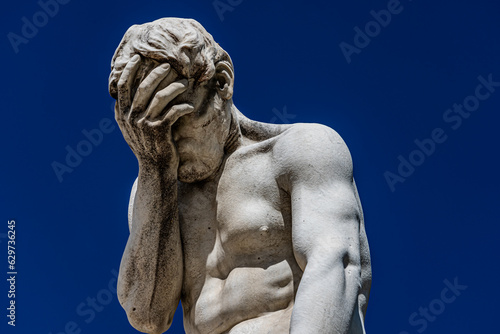 Paris, France - 15 September 2022: Sad and frustrated man face palm white sculpture on the blue clear sky background photo