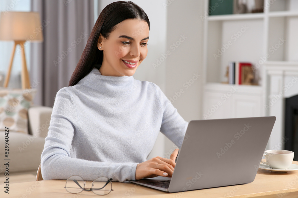 Happy woman working with laptop at wooden desk in room Happy woman working with laptop at wooden desk in room