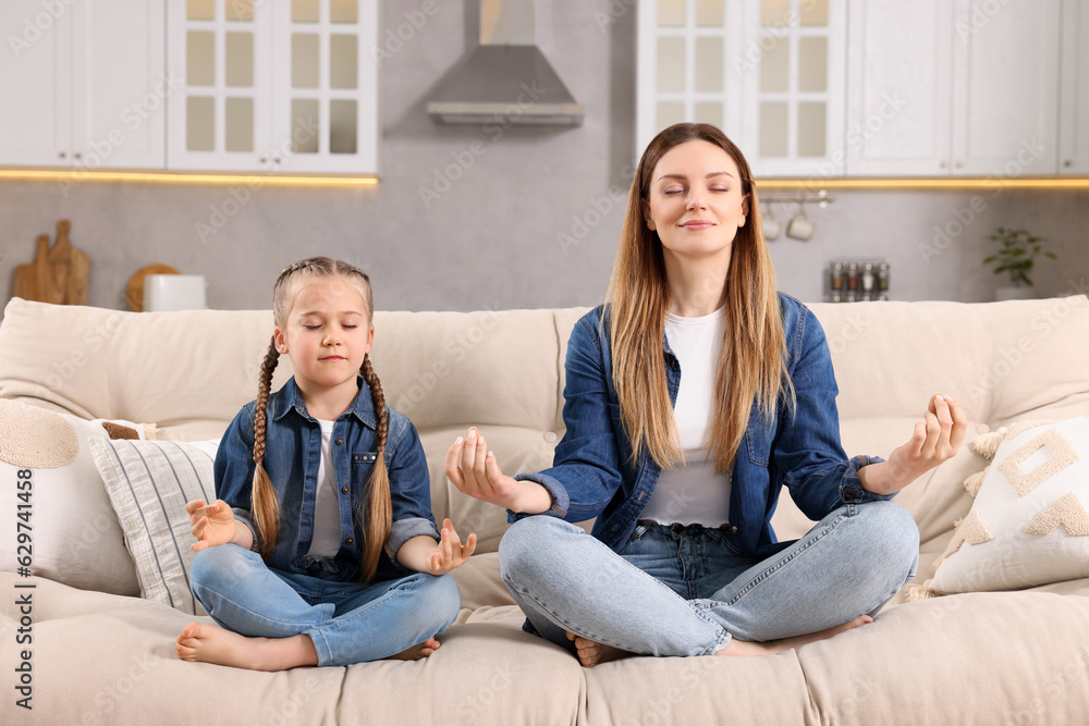 Mother with daughter meditating on sofa at home. Harmony and zen Mother with daughter meditating on sofa at home. Harmony and zen