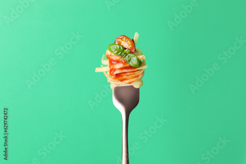 Tasty pasta with tomato sauce and basil on fork against green background