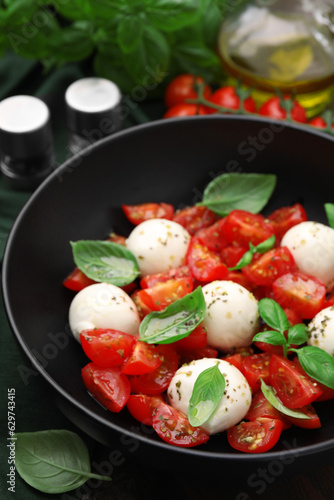 Tasty salad Caprese with tomatoes, mozzarella balls and basil on table, closeup