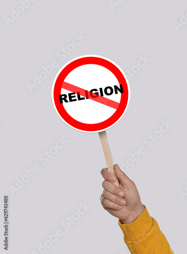 Atheism concept. Man holding prohibition sign with crossed out word Religion on light grey background
