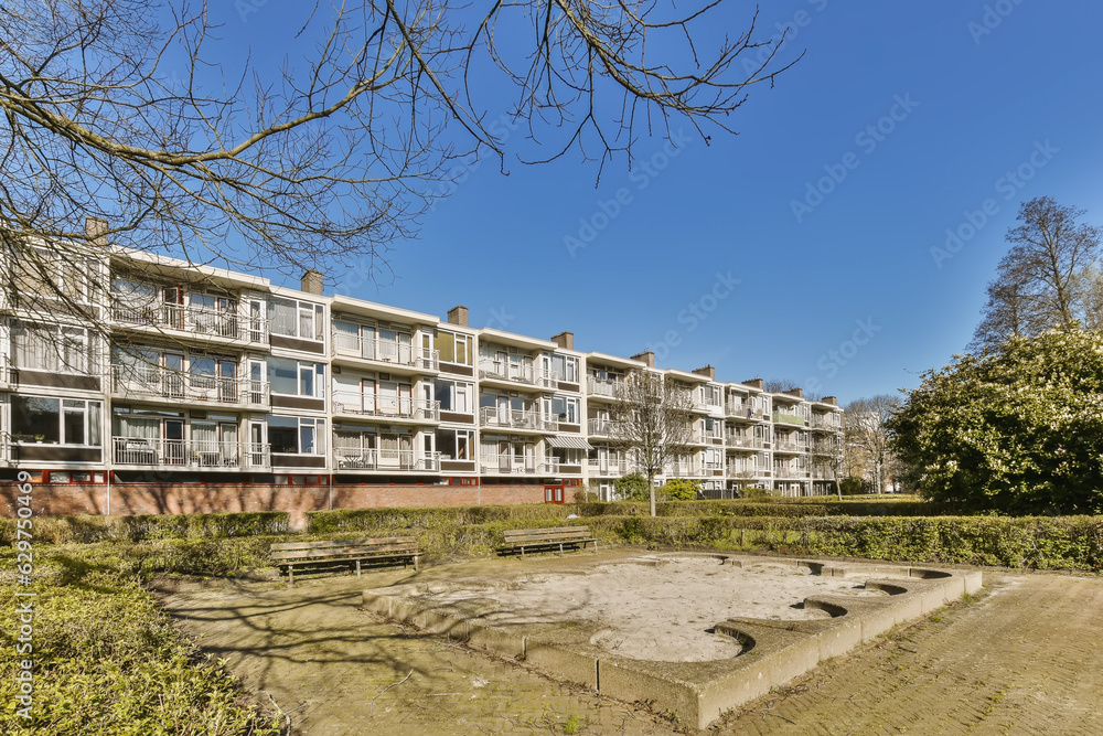 an apartment complex with trees and bushes in the foreground area on a clear blue sky day - stock photo