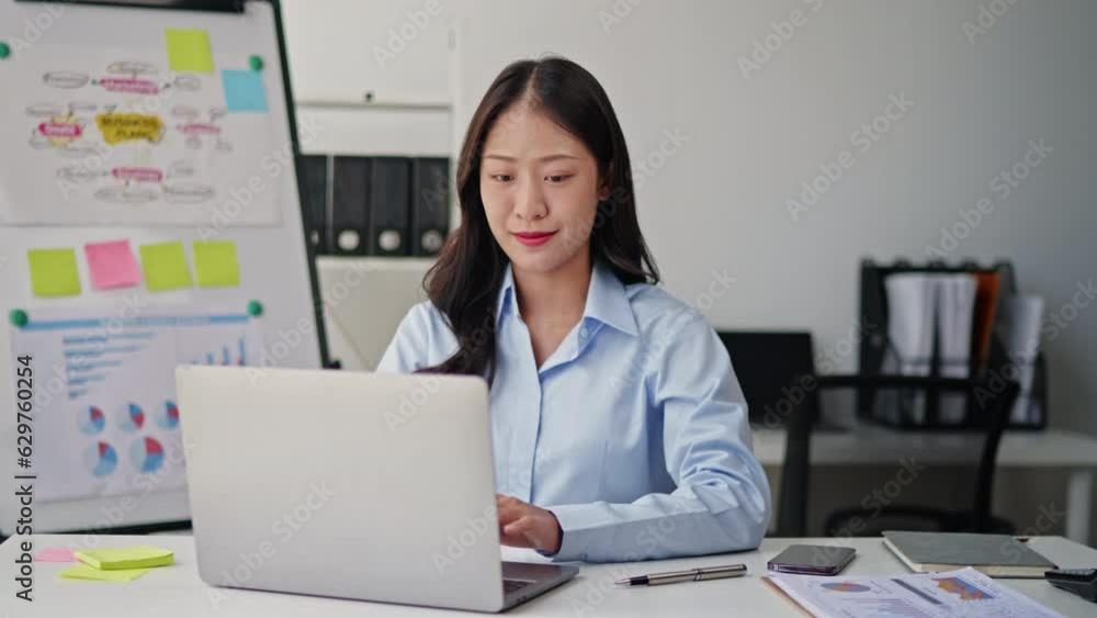 Businesswoman in blue sky shirt is working on laptop and paperwork that show cost planning accounting numbers tables on office space. Businesswoman in blue sky shirt is working on laptop and paperwork that show cost planning accounting numbers tables on office space.