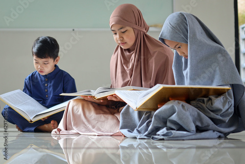 Group of muslim children sitting on the floor inside mosque and reading Quran together during Ramadan.  photo