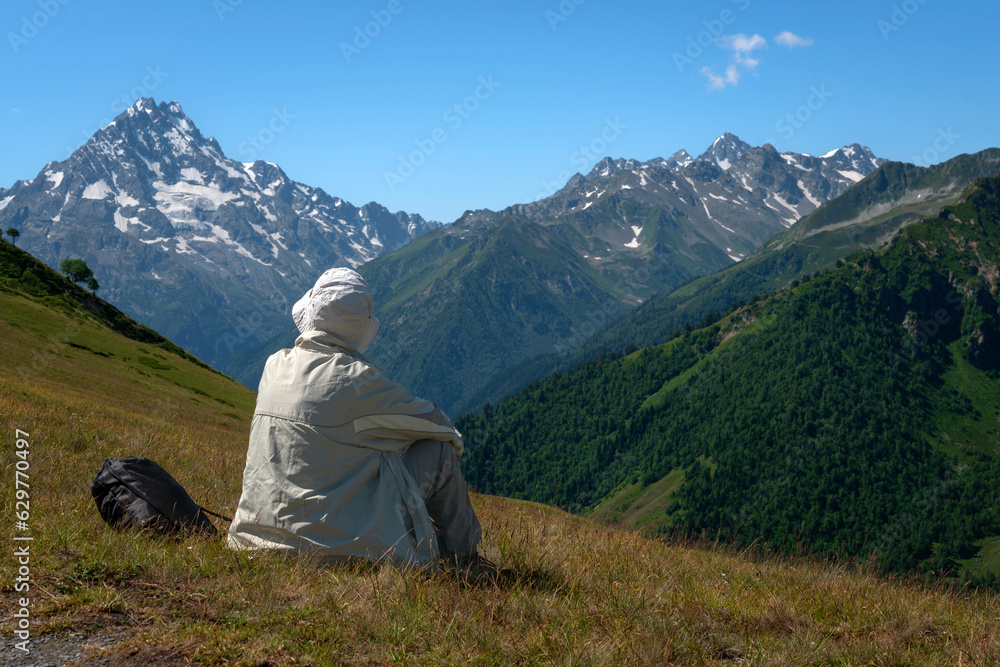 View of a tourist resting on a mountain slope in the North Caucasus with a view of the top of the mountain Pshish on a sunny summer day, Arkhyz, Karachay-Cherkessia, Russia