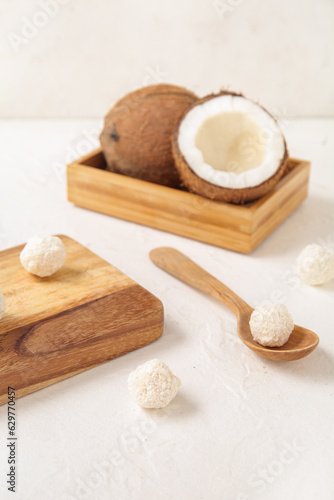 Wooden board and spoon with delicious coconut candies on white table