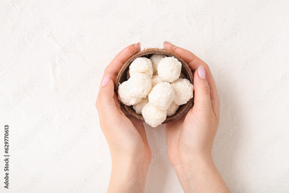 Woman holding coconut shell with white chocolate candies on light background Woman holding coconut shell with white chocolate candies on light background