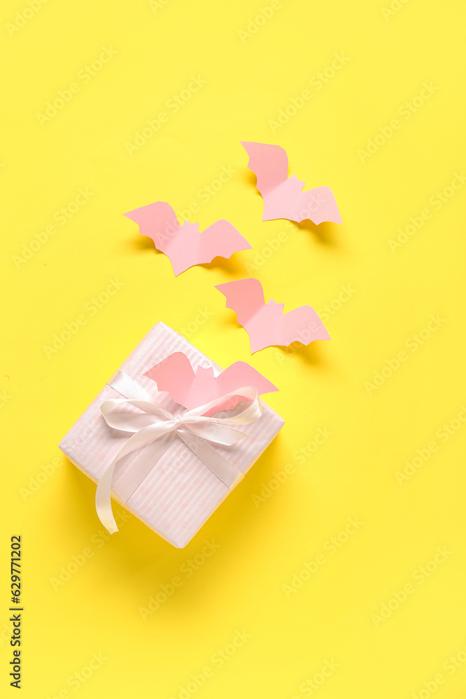 Composition with beautiful gift box and bats made of paper for Halloween on yellow background Composition with beautiful gift box and bats made of paper for Halloween on yellow background
