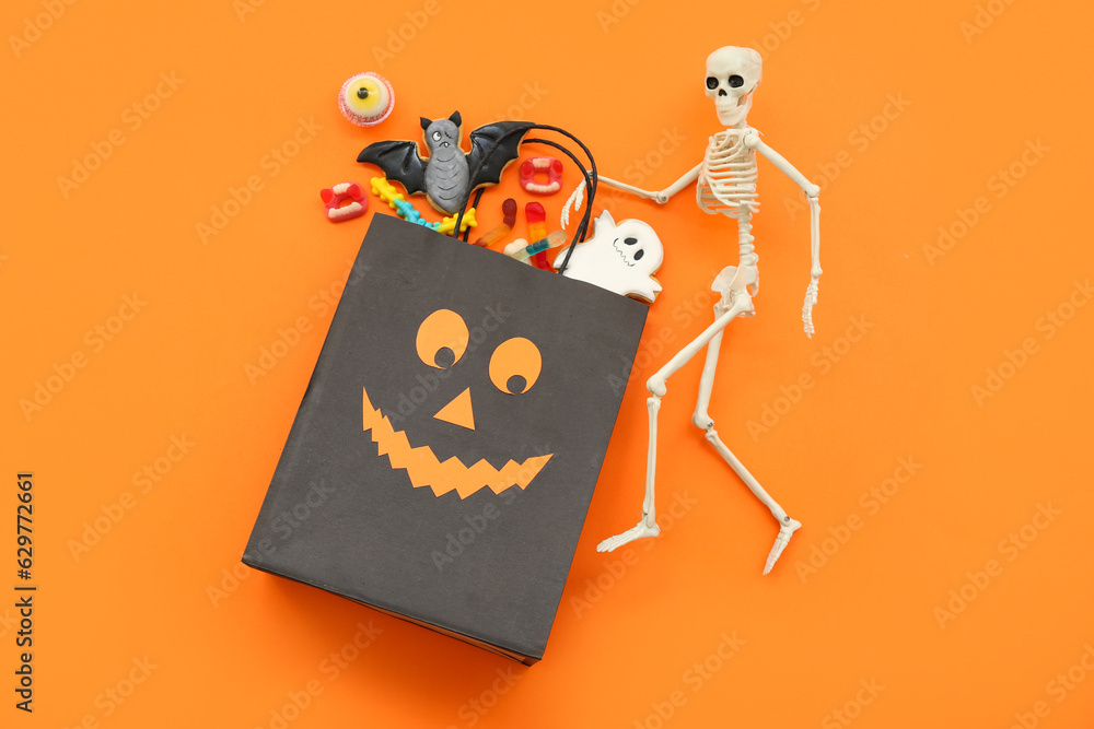 Composition with shopping bag, skeleton, tasty cookies and candies for Halloween on orange background