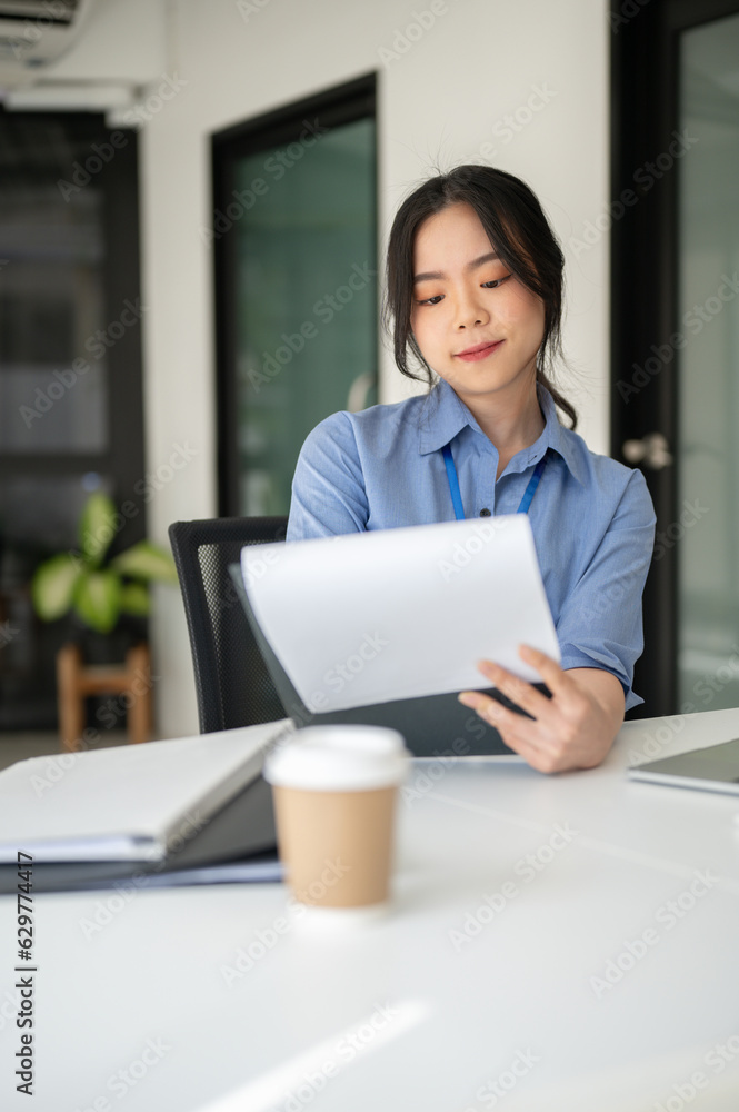 An attractive Asian female office worker is examining business documents at her desk An attractive Asian female office worker is examining business documents at her desk