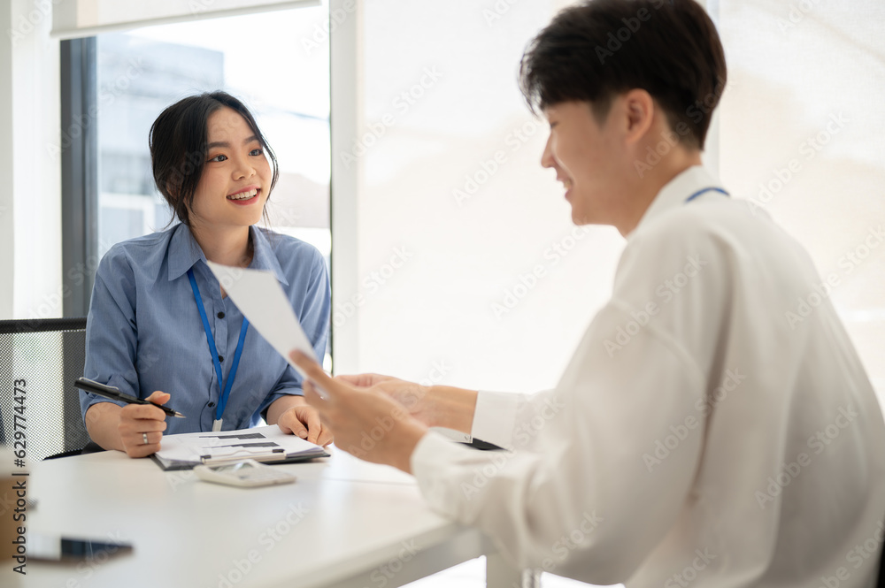 A happy Asian female office worker is discussing work, brainstorming with a male colleague A happy Asian female office worker is discussing work, brainstorming with a male colleague