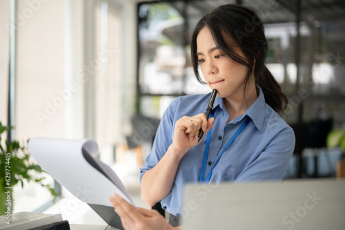 A focused and smart Asian businesswoman is reading and examining business documents