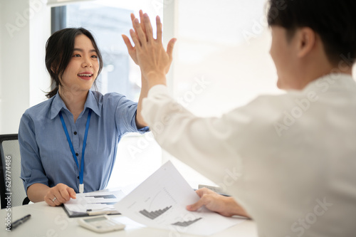 Obraz na plátně A cheerful Asian businesswoman gives high fives to a male colleague while working together