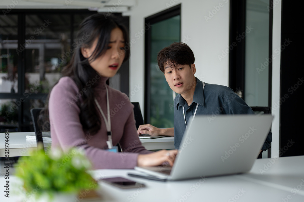 A smart Asian male office worker is trying to help a stressed female colleague with laptop problems. A smart Asian male office worker is trying to help a stressed female colleague with laptop problems.